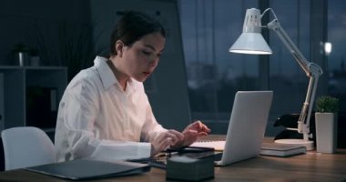 İş kadını laptopta çalışıyor ve gece ofisindeki cep telefonuyla sesli mesaj gönderiyor.