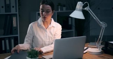 İşkadını dizüstü bilgisayar kullanıyor ve geç saatlerde ofiste evrak işleriyle uğraşıyor.