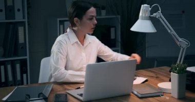 İş kadını gece ofisinde çalışırken cep telefonuyla konuşuyor.