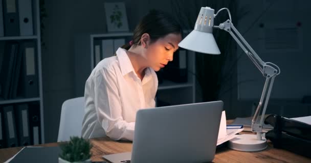 Businesswoman using laptop and writing notes at night office — Stock Video