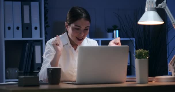 İş kadını laptoptaki işini bitirip gece ofisten çıkıyor. — Stok video