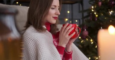 Evde battaniyeye sarılı sıcak kahve içen bir kadın.