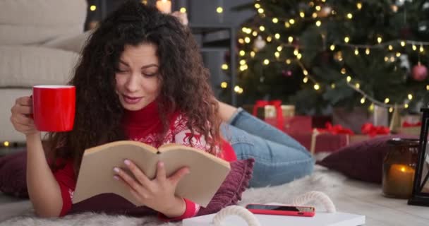 Vrouw die boek leest en koffie drinkt op kerstavond — Stockvideo