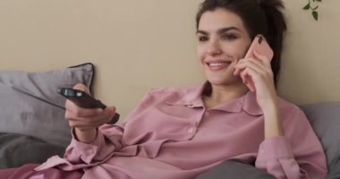 Evde televizyon izlerken cep telefonuyla konuşan bir kadın.