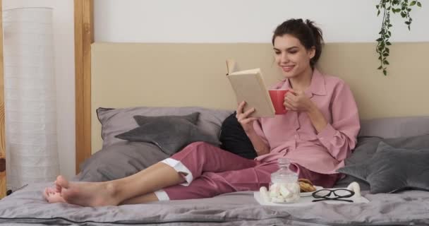 Mujer leyendo libro y tomando café en la cama — Vídeo de stock