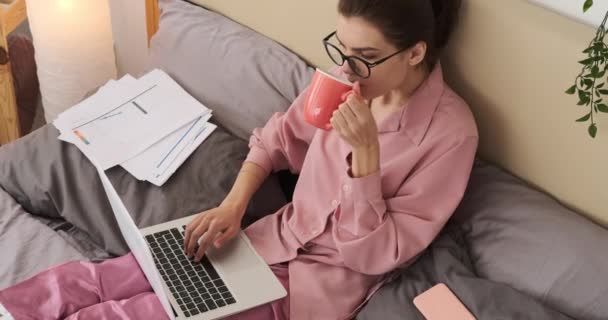 Kvinna dricka kaffe och analysera dokument i sängen — Stockvideo