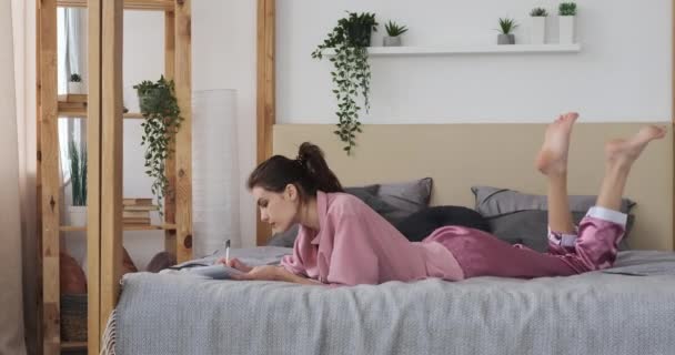Kvinna skriver i anteckningsblock avkopplande på sängen hemma — Stockvideo