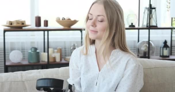 Женщина слушает музыку с помощью наушников на диване — стоковое видео