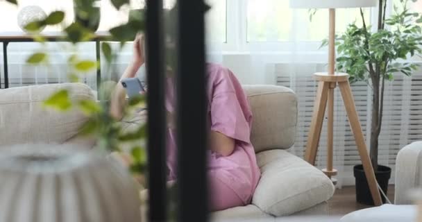 Femme heureuse utilisant un téléphone mobile sur le canapé à la maison — Video