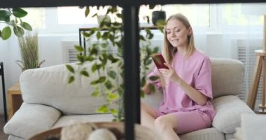 Mutlu kadın evdeki koltukta cep telefonu kullanıyor.