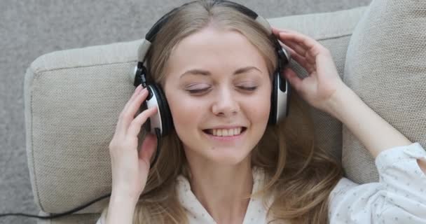 Donna che ascolta musica usando le cuffie sul divano — Video Stock