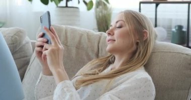 Mutlu kadın evdeki koltukta cep telefonu kullanıyor.