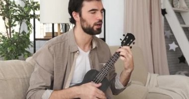 Adam evde şarkı söylüyor ve gitar çalıyor.