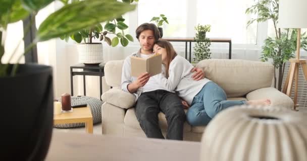 Ο άνθρωπος διαβάζει βιβλίο στη σύζυγο αναπαύεται στο σπίτι — Αρχείο Βίντεο