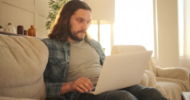 Чоловік використовує ноутбук на дивані вдома — стокове відео
