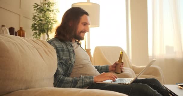 Hombre usando laptop y bebiendo cerveza en casa — Vídeo de stock