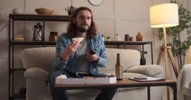 Pizzayı ve birayı seven bir adam evde televizyon izliyor.