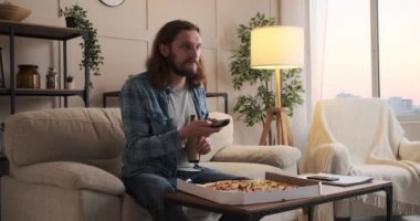Pizzayı ve birayı seven bir adam evde televizyon izliyor.