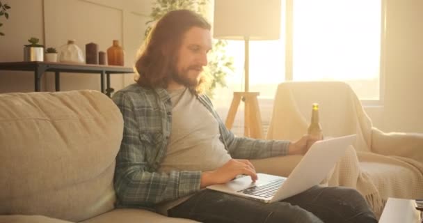 Hombre usando laptop y bebiendo cerveza en casa — Vídeo de stock