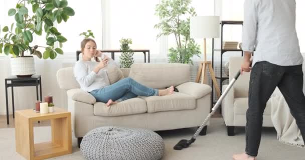 Mujer bebiendo vino en el sofá mientras su marido está aspirando alfombras — Vídeo de stock