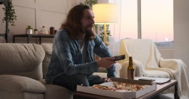 Pizzayı ve birayı seven bir adam evde televizyon izliyor.