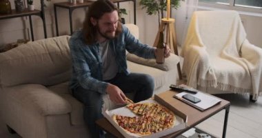 Pizzayı ve birayı seven bir adam evde televizyon izliyor.