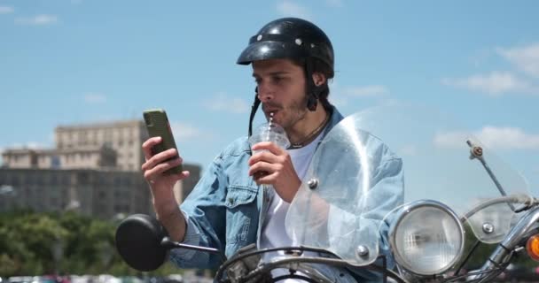 Man drinking juice and using mobile phone on motorcycle — Stock Video