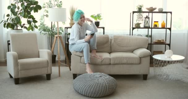 Mensajería de texto mujer feliz usando el teléfono móvil en el sofá en casa — Vídeos de Stock