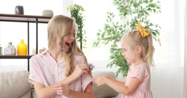 Маленькая девочка укладывает волосы своей матери дома — стоковое видео
