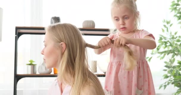 Petite fille faisant tresse de cheveux de sa mère à la maison — Video