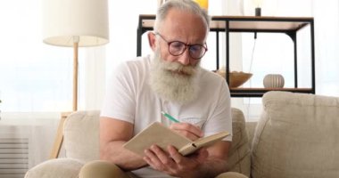 Yaşlı adam bir kitap okurken kalemle işaretliyor.