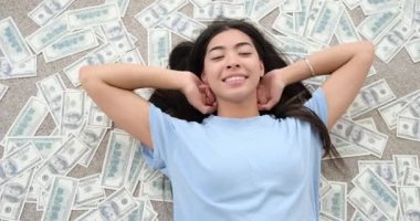 Kadın etrafa saçılmış nakit dolarların üzerine yatıyor.