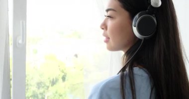 Müzik dinleyen ve pencereden dışarı bakan bir kadın.