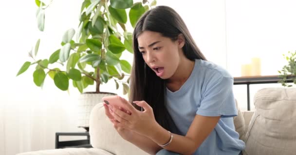 Женщина расстроена, когда читает плохие новости, используя мобильный телефон дома — стоковое видео