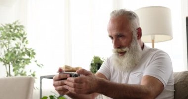 Yaşlı adam evde cep telefonu kullanarak oyun oynuyor.