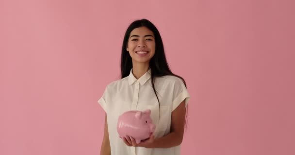 Lächelnde Frau steckt Münze in Sparschwein — Stockvideo