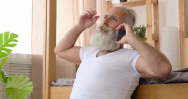 Yaşlı adam evde cep telefonuyla konuşuyor.