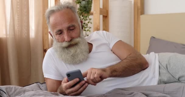 Viejo usando teléfono móvil en la cama — Vídeos de Stock