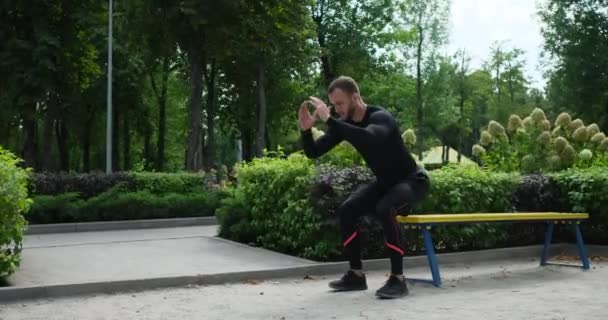 Sportowiec siedzi na ławce i skacze w parku — Wideo stockowe