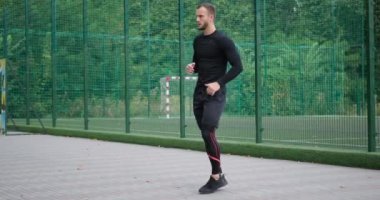 Sporcu yerinde koşuyor ve bacaklarını açıyor.