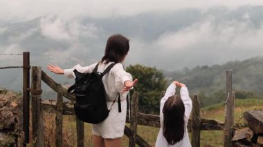 Kırsal kesimde, sisli bir dağ manzarasını işaret eden bir anne ve kızın arka görüntüsü..
