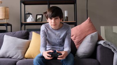 Oturma odasındaki kanepede otururken video oyunu oynayan bir gencin orta ölçekli görüntüsü..