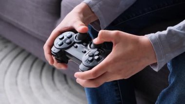 Evdeki bir kanepede otururken, genç bir çocuğun elleri kablosuz oyun kumandası kullanıyor..