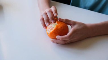 Beyaz bir masada taze portakalı elle soyan bir gencin yakın çekimi..
