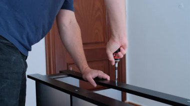 Yetişkin bir adam, evde siyah bir raf ünitesi monte ederken, cırcırböceği sürücüsü ile vidayı sıkıyor..