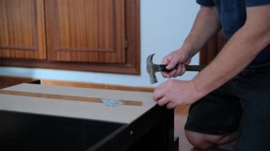 Yetişkin bir adam diz çöker ve arka paneli evdeki siyah bir rafa takmak için çiviler..