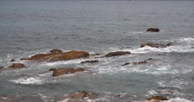 Okyanus ve deniz dalgalarının kıyı şeridi manzarası köpüklü beyaz suyla kayalık kıyı oluşumlarını kaplıyor..