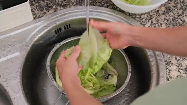 Yetişkin bir kadının mutfak lavabosunda akan suyun altında marul yapraklarını durulaması..