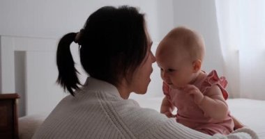 Yavru kızına sarılıp burunlarını okşayan bir annenin yavaş çekimde yatakta otururken....