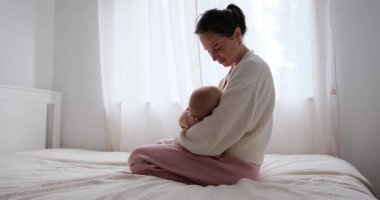 Yavru kızını yatakta emziren bir annenin yavaş çekimde orta ölçekli fotoğrafı..